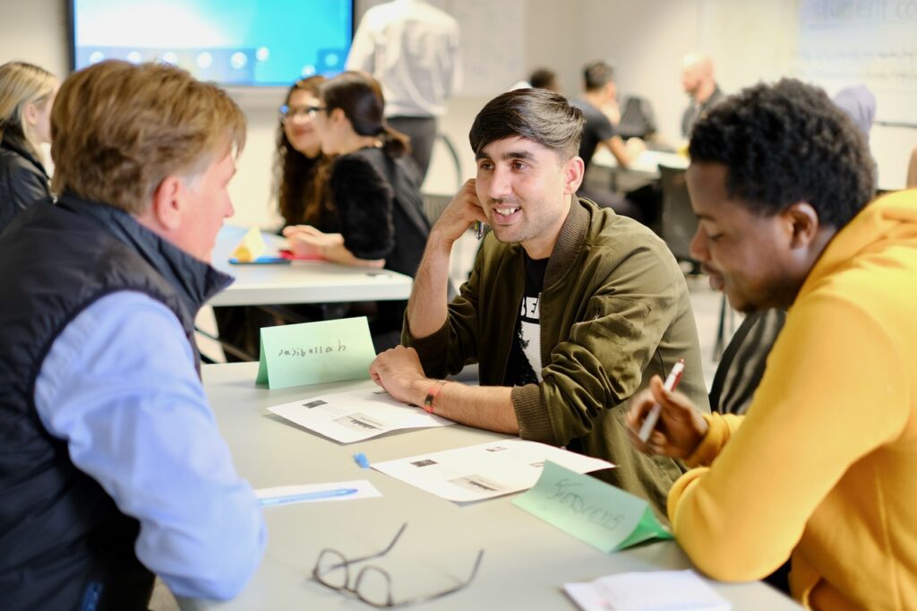 A tutor and two students sit opposite at a table.