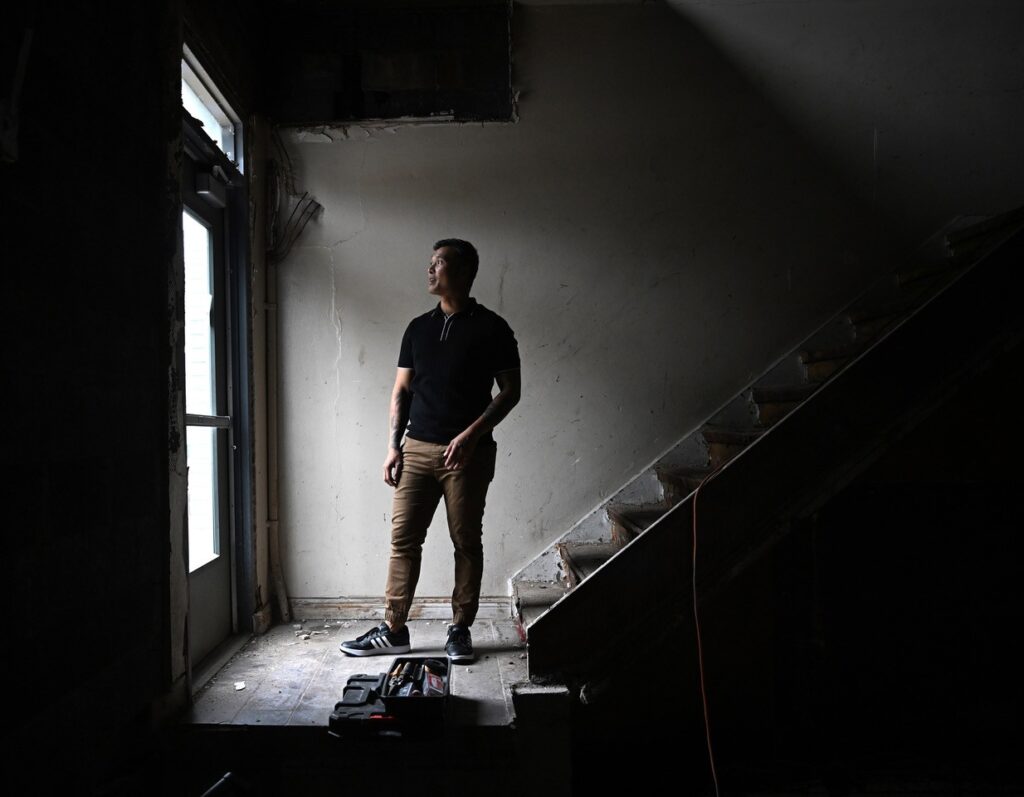Rafeal stands in a dark entry way with a stair case behind him.