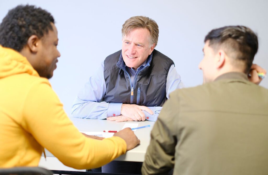 An instructor in focus with two students in front of him talking