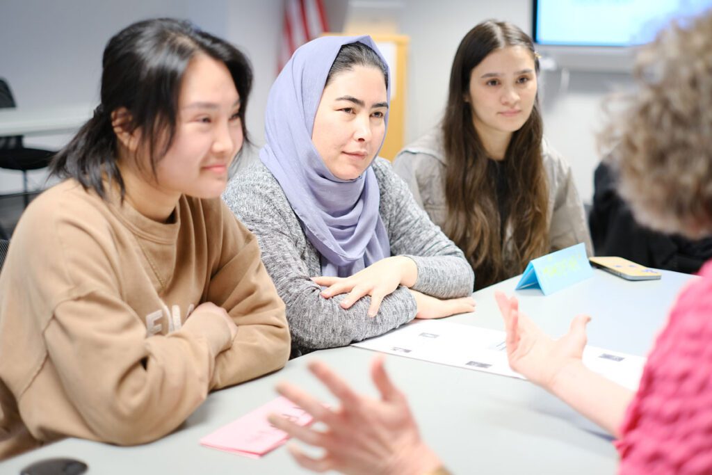 3 students sitting at a table listening to their instructor