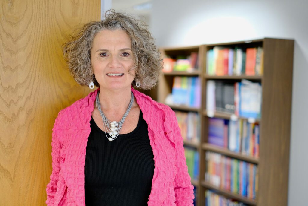 Mhra pictured in a bright pink sweater standing in front of book shelves