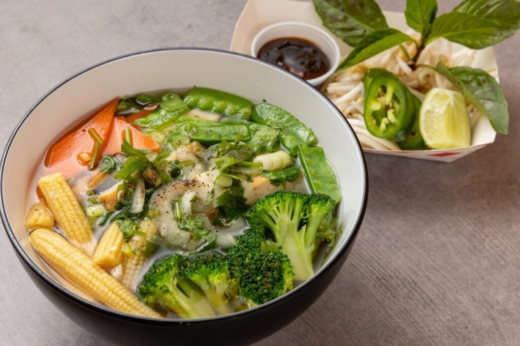 A dish of vegetarian pho with carrots, broccoli, and corn. 