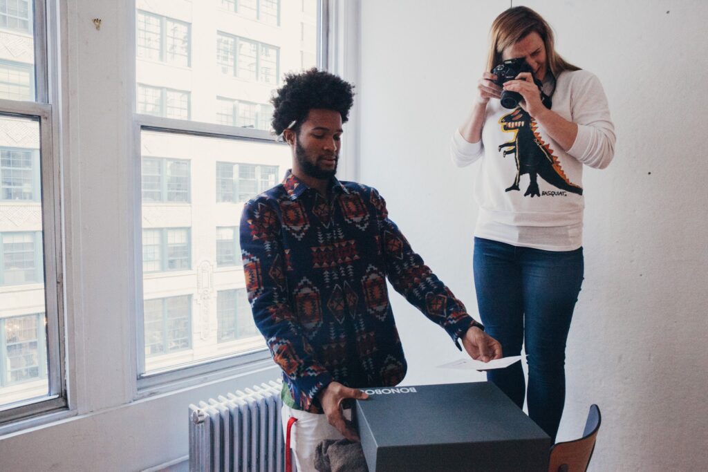 A woman takes a photo of a colleague showing off brand packaging and product