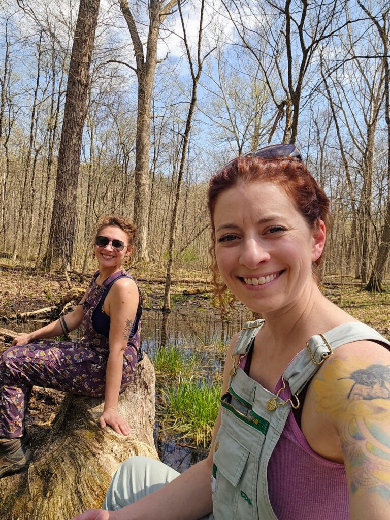 Michelene sits on a log with her sister in the woods after a hike. 