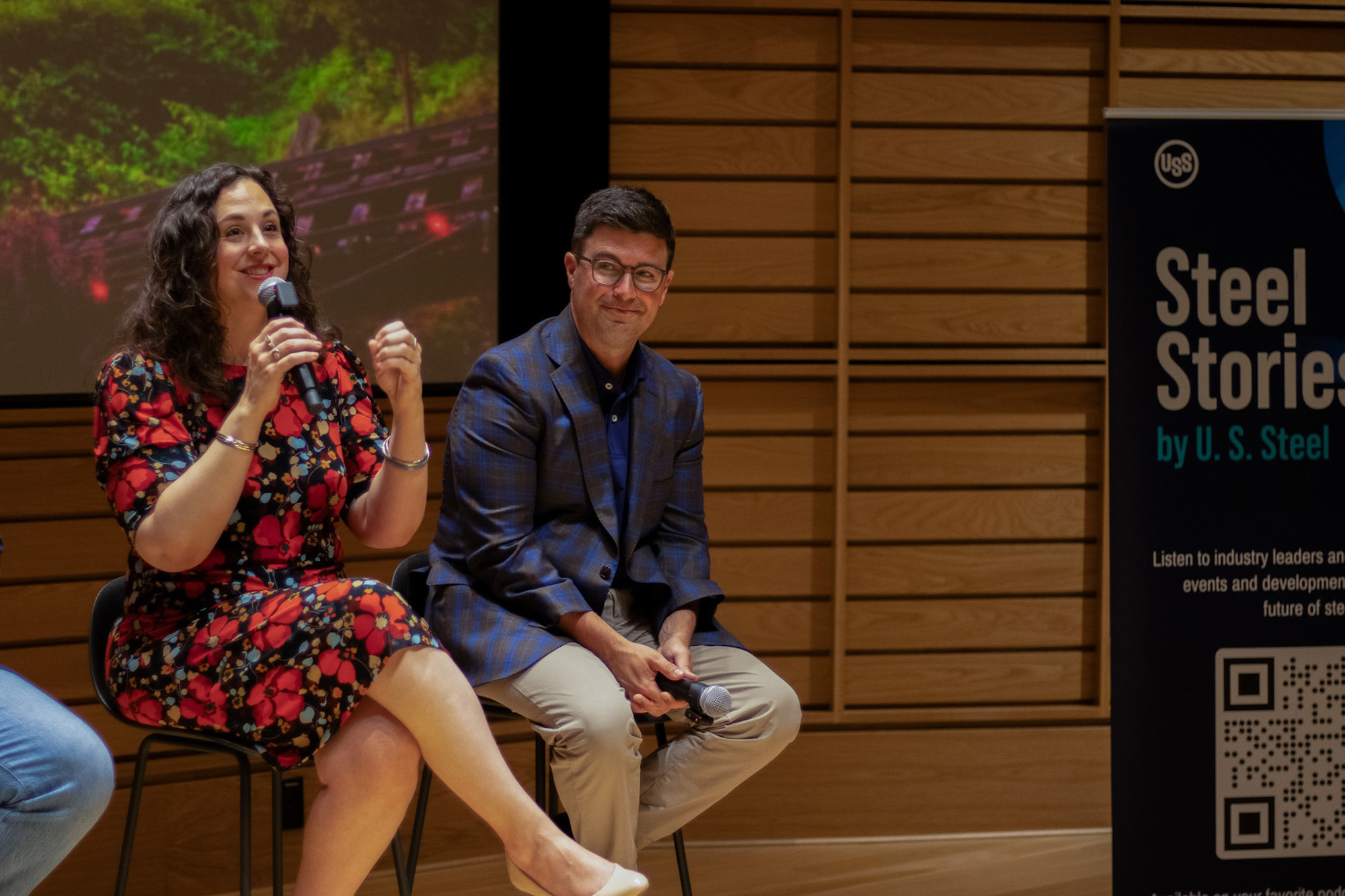 A woman speaking with a microphone as a man smiles and watches her speak.