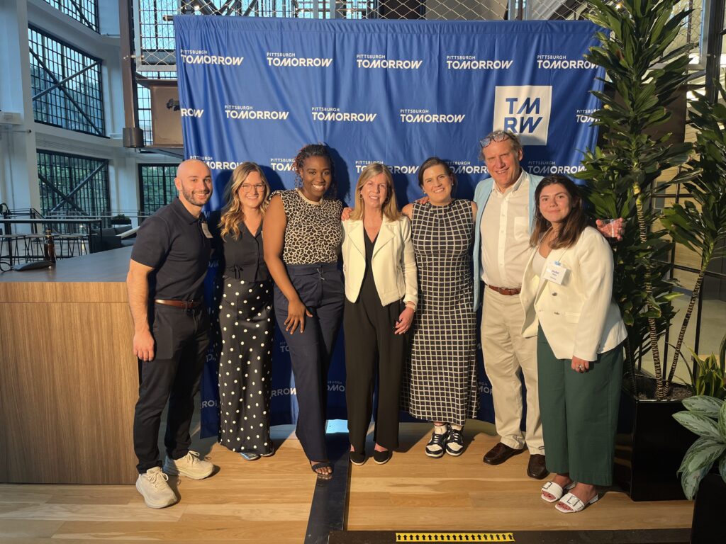 Scott, Haley, Feyi, Linda, Caroline, Doug, and Isabel at the Intersection Event in May, standing in front of a Pittsburgh Tomorrow backdrop. 