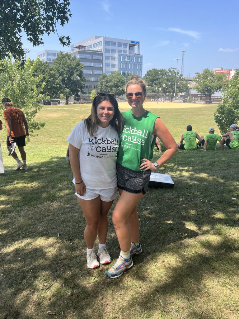 Isabel and Alyssa are together at the Kickball for a cause Tournament, standing on the field.